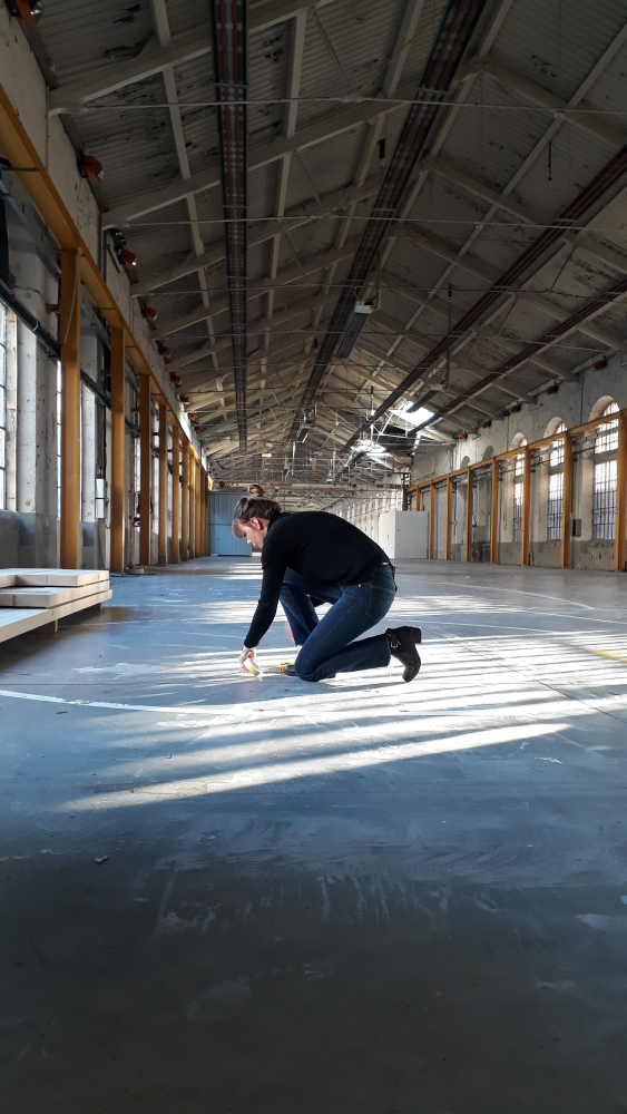 Une jeune femme dessine des lignes droites sur le sol de l'atelier.